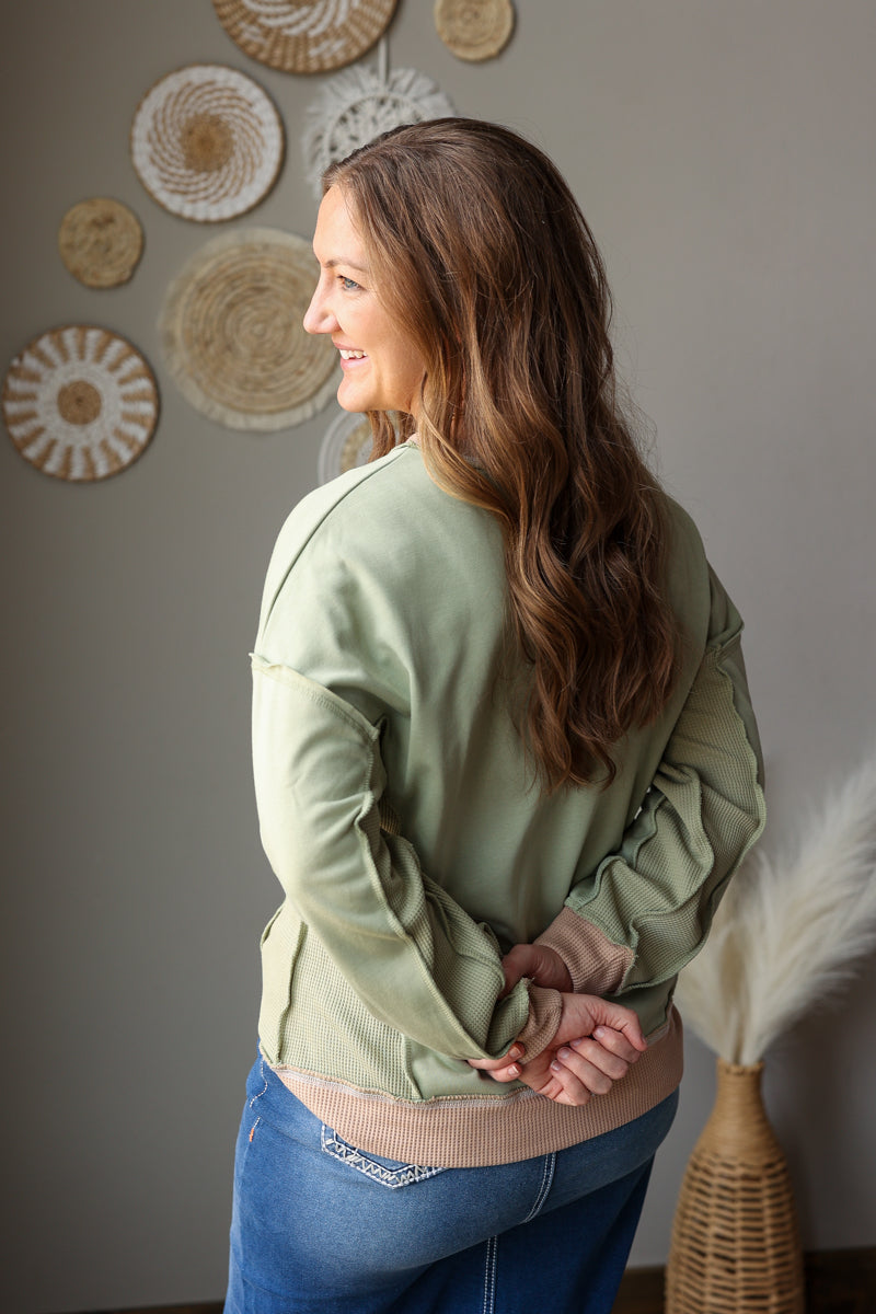 Woman wearing a green top and blue jean skirt standing in a room with decorative wall art.