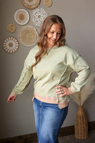 Woman wearing a light green top and blue jean skirt standing in a room with decorative wall art.