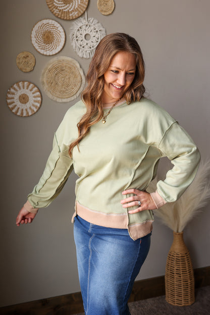 Woman wearing a light green top and blue jean skirt standing in a room with decorative wall art.