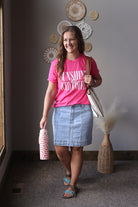 Woman in pink shirt and denim skirt standing indoors with decorative wall art in the background