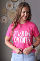 Woman wearing a pink t-shirt with 'Sunshine and iced coffee' text, standing against a neutral wall.