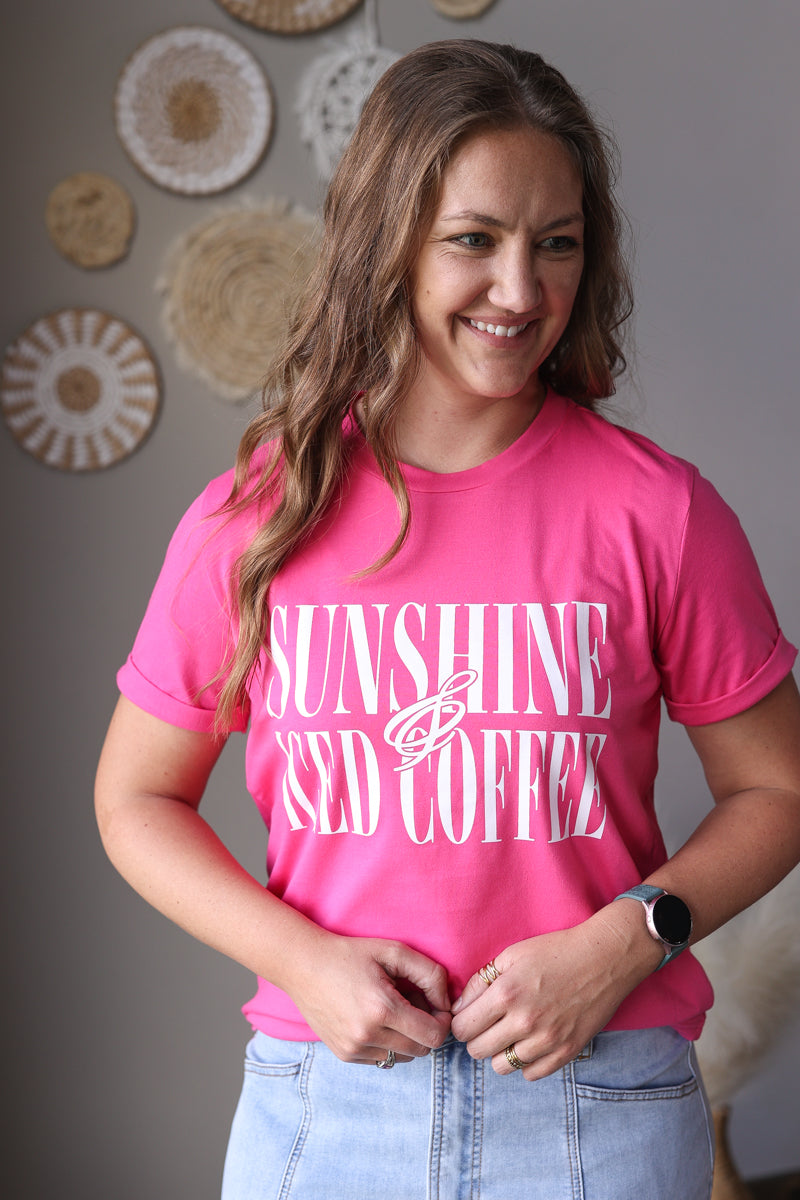 Woman wearing a pink t-shirt with 'Sunshine and iced coffee' text, standing against a neutral wall.