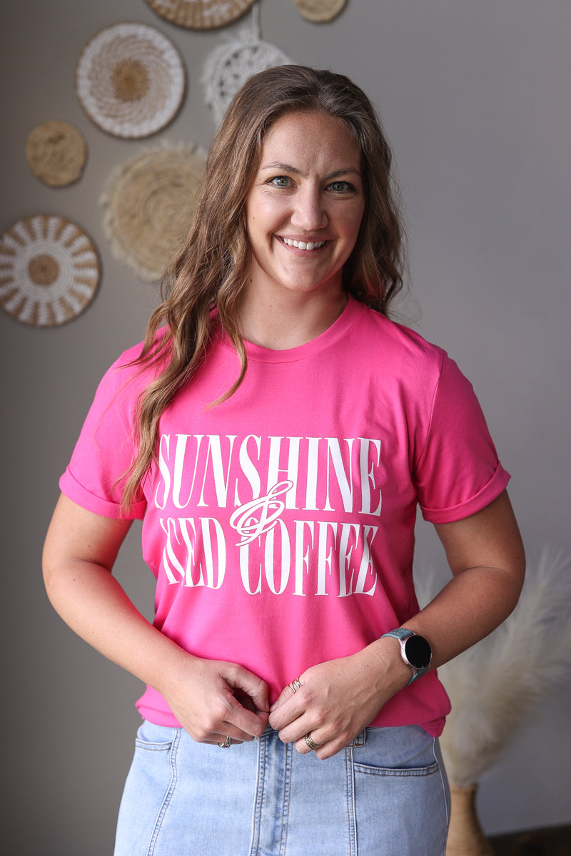 Woman wearing a pink t-shirt with 'Sunshine and Iced Coffee' text, standing against a neutral wall.