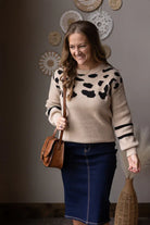 Woman wearing a beige sweater with black patterns and a blue skirt, holding a brown bag. Cute Modest Mom Sweater for Fall Winter 2025.