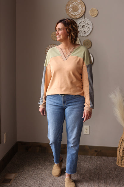 Woman wearing a colorblock vneck top and blue jeans standing in a room with decorative wall hangings for a cute easy fall winter outfit.