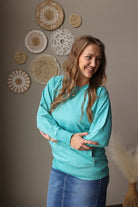 Woman wearing a turquoise sweater and blue jeans standing in front of decorative wall art.