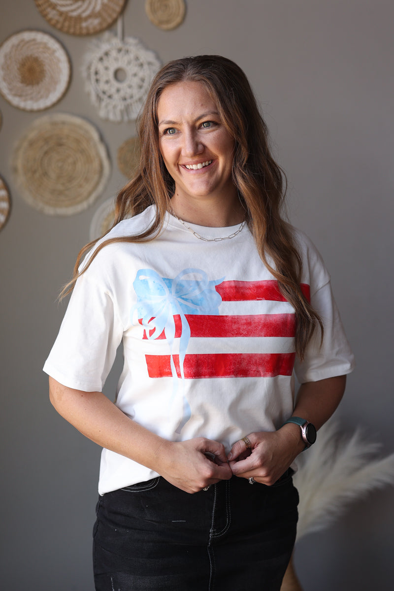 Woman wearing a white t-shirt with a graphic design, standing against a neutral wall.