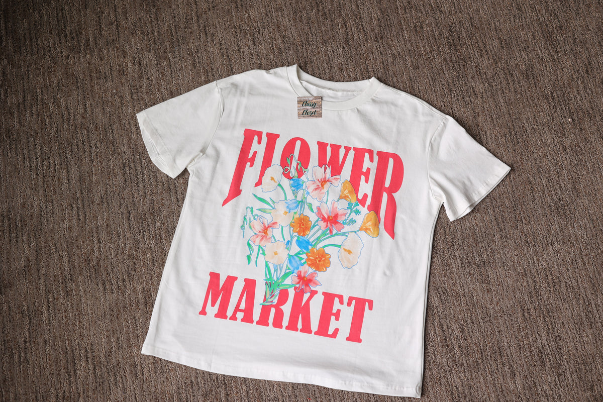 White t-shirt with 'Flower Market' text and floral design on a brown surface