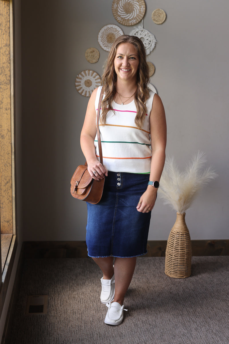 Woman in a striped top and denim skirt standing indoors with decorative elements on the wall.