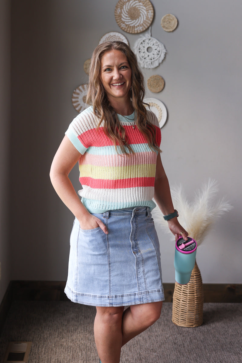 Woman wearing a colorful striped shirt and denim skirt standing in a room with decorative wall art.