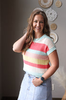Woman wearing a colorful striped sweater and light blue jeans indoors.