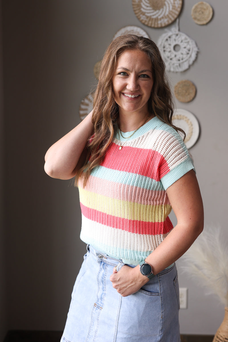 Woman wearing a colorful striped sweater and light blue jeans indoors.