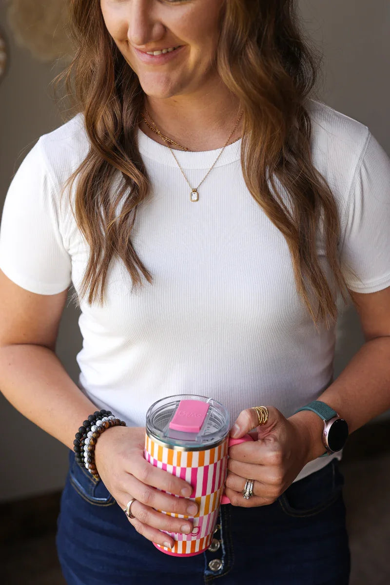 Woman holding a striped tumbler with a pink lid indoors