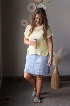 Woman in a yellow top and denim skirt holding a coffee cup indoors.